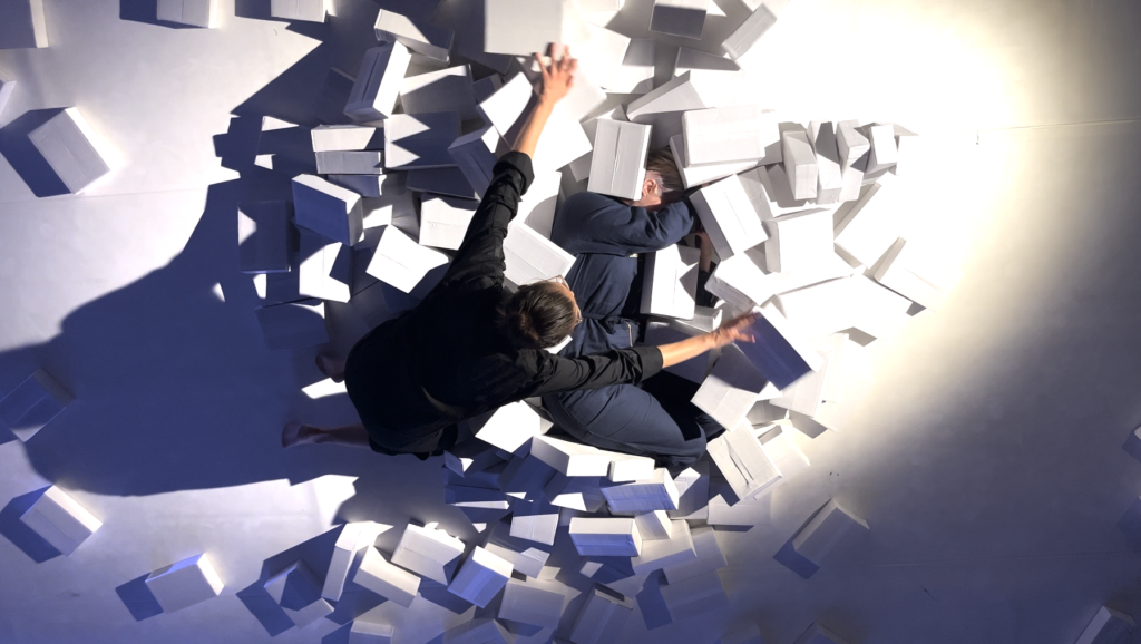 two people performing on the floor among cardboard boxes